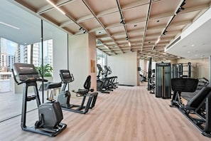 Une salle de sport équipée de machines de cardio, d’appareils de musculation et dotée d’une grande fenêtre offrant une vue sur la ville.