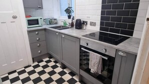 Cozinha compacta com armários cinza, piso quadriculado preto e branco, micro-ondas, torradeira e painel de azulejos pretos.