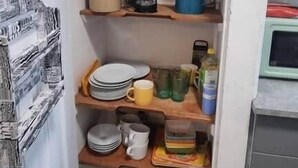 Uma cozinha com piso xadrez, geladeira e prateleiras com pratos e utensílios.