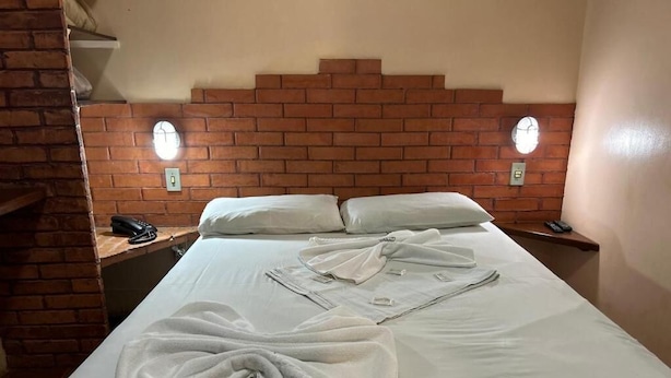 A hotel room with a brick headboard, a bed with white linens, two bedside tables with lamps, and a phone on one of the tables. - Goiânia Palace Hotel (Goiânia)
