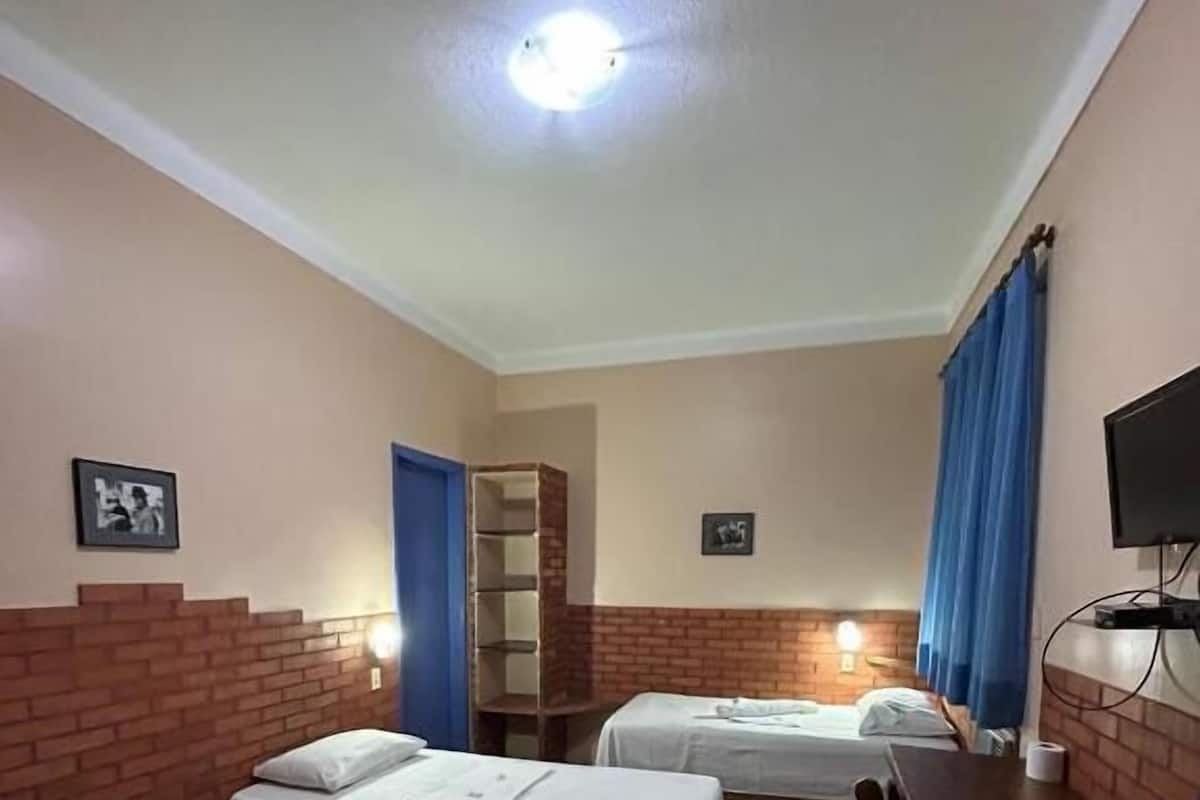 A hotel room with three single beds, a desk, a television, and a brick accent wall.