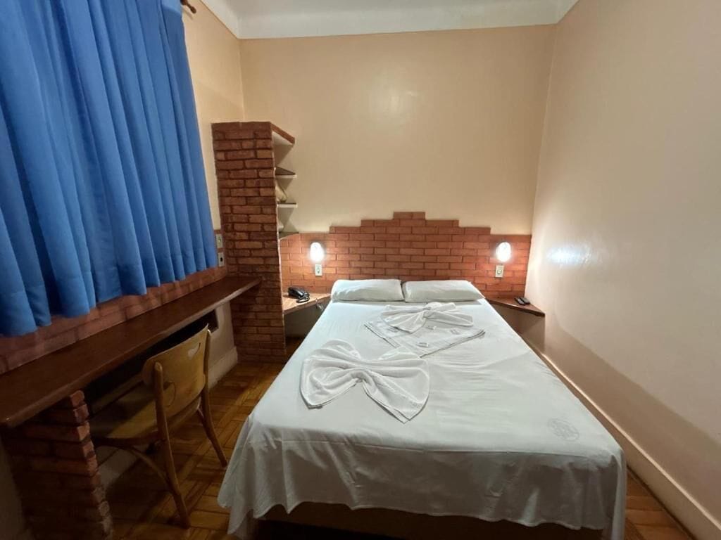Une chambre d’hôtel avec un lit, un bureau et une chaise. On y trouve deux lampes de chevet et un mur décoratif en briques.