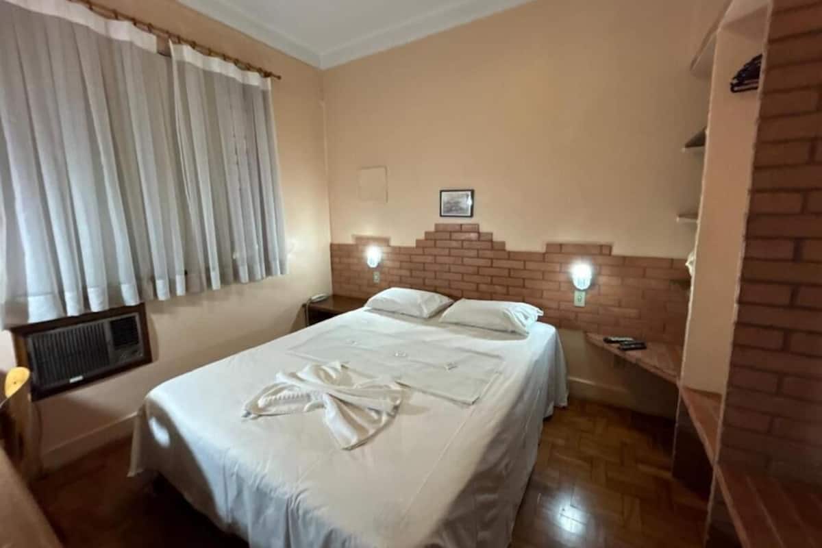 A bedroom with a large bed, a brick accent wall, and a window with curtains.