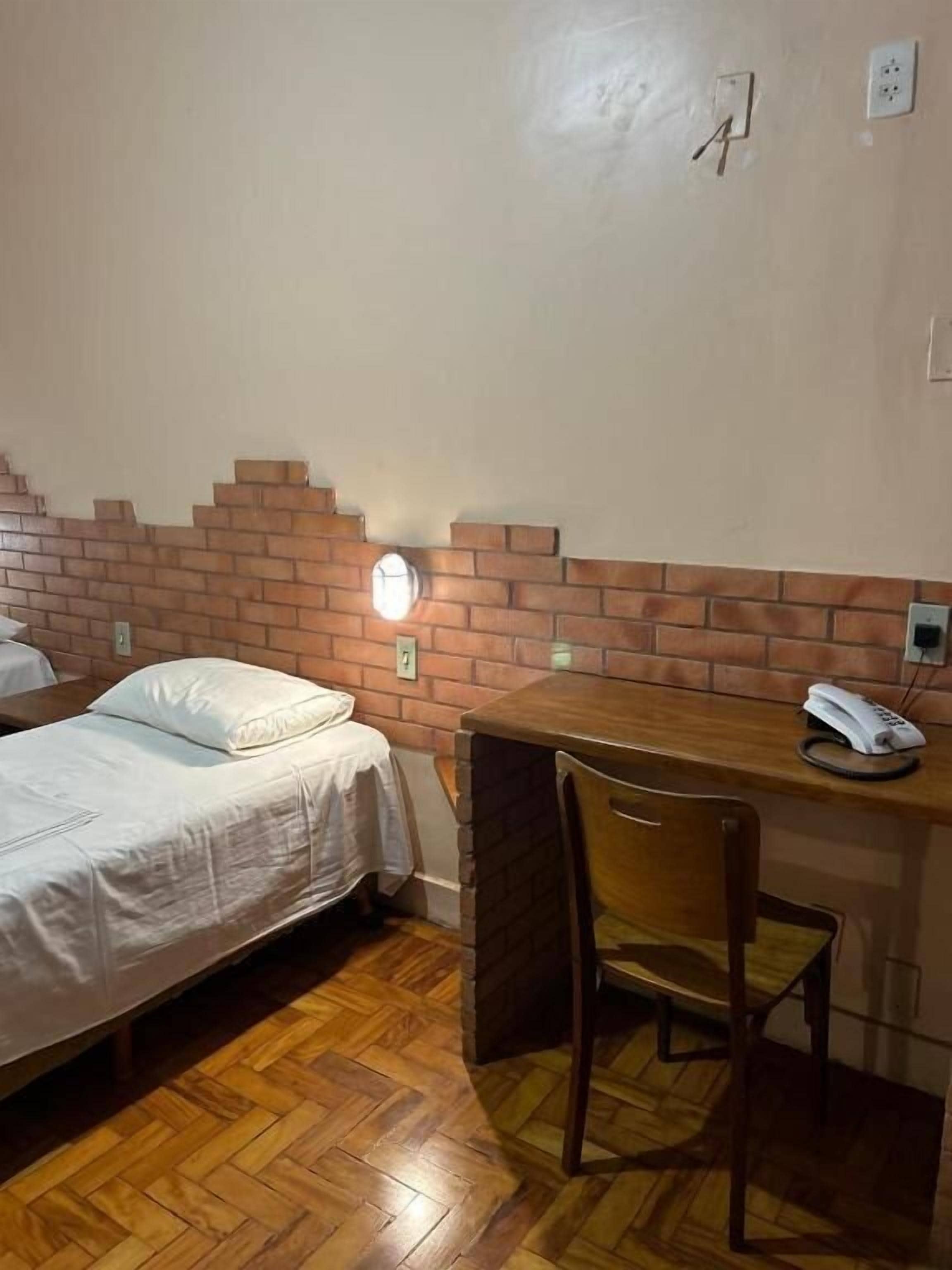 Une pièce comprenant un lit, un bureau, une chaise, un téléphone et une lampe fixée au mur.