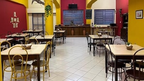 A dining area with tables and chairs, a counter, and a red wall with framed pictures. - Goiânia Palace Hotel (Goiânia)