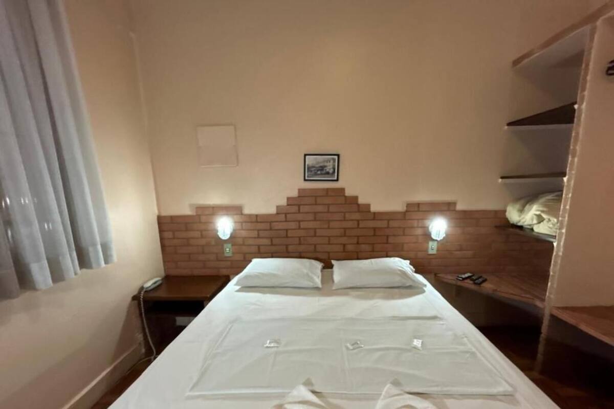 A hotel room with a large bed, two bedside tables, a brick-patterned headboard, and a small picture on the wall.