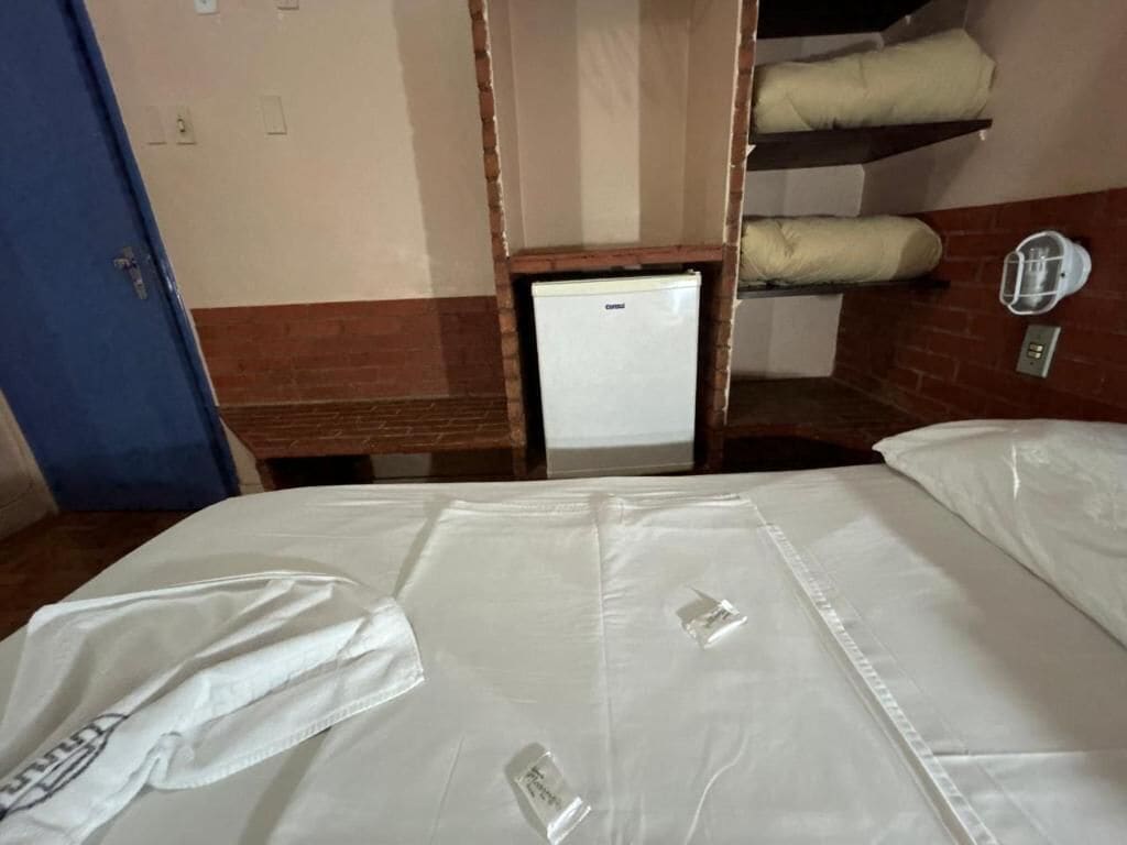A hotel room with a bed, a small refrigerator, and bunk beds in the background.