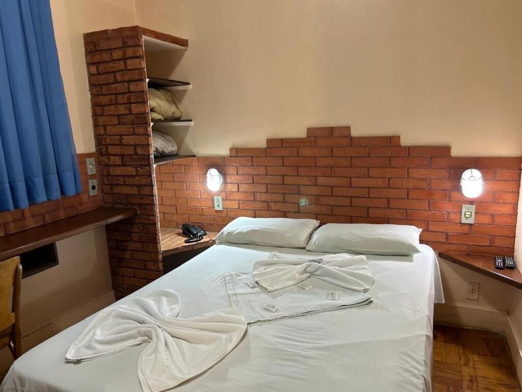 Habitación de hotel con cabecera de ladrillo, cama con ropa blanca y bata sobre la cama.