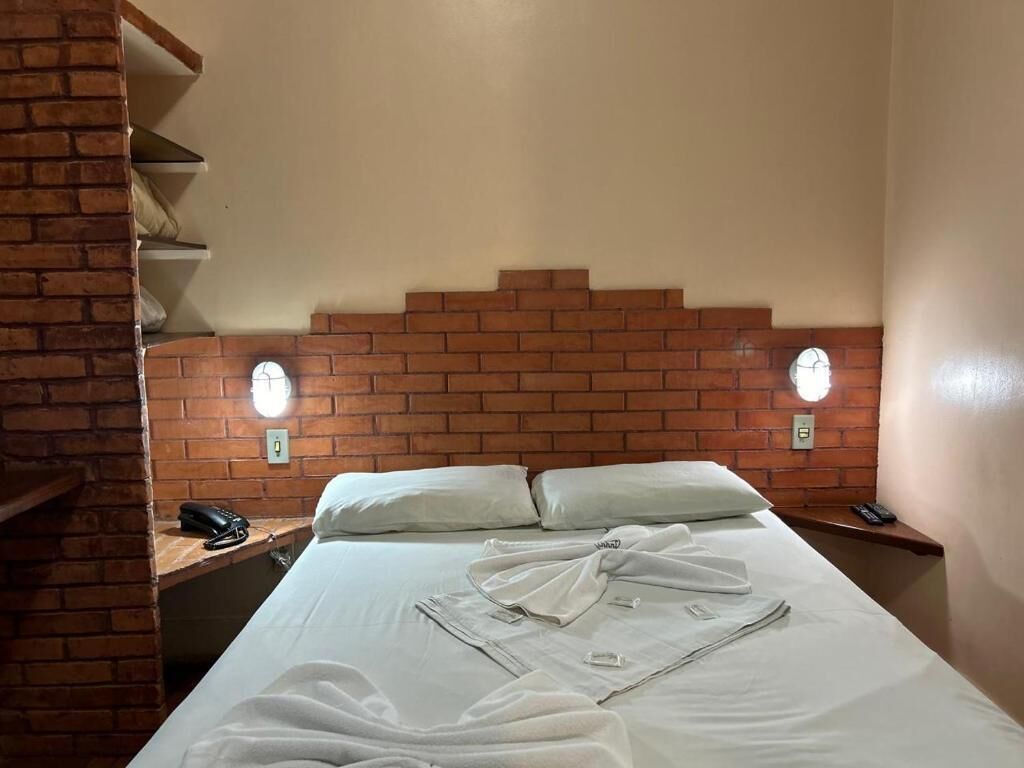 A hotel room with a brick headboard, a bed with white linens, two bedside tables with lamps, and a brick wall.