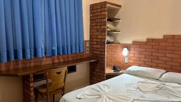 Habitación de hotel con cabecera de ladrillo, escritorio con silla, cama con ropa blanca y cortina azul.