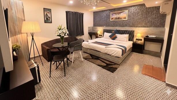 Ein modernes Hotelzimmer mit einem großen Bett, einem Schreibtisch, einem Sessel, einer Chandelierleuchtre und einem kleinen Tisch mit Blumen.