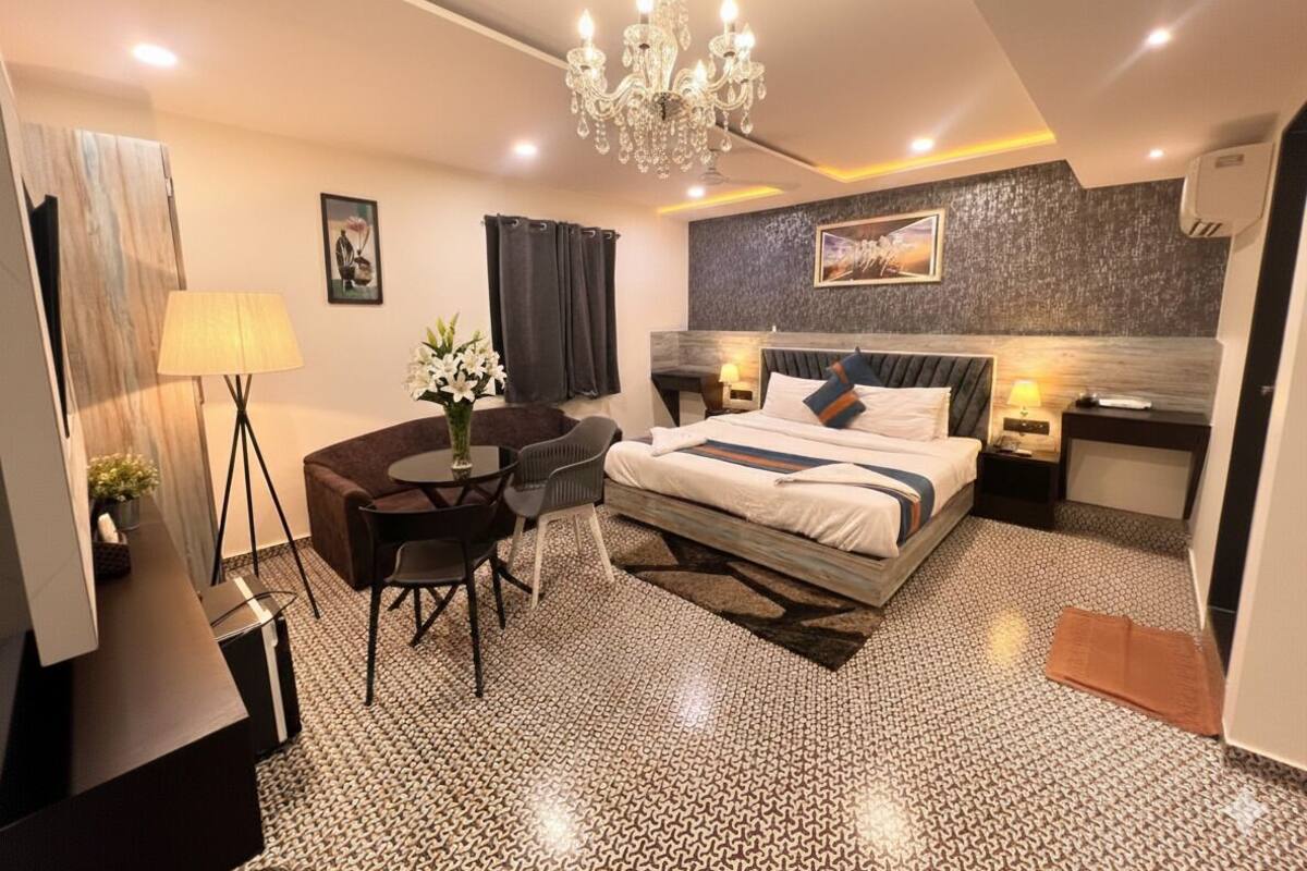 Una habitación de hotel moderna con una cama grande, un escritorio, una silla, una araña y una mesita con un jarrón de flores.