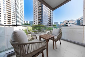 A balcony with wicker chairs and a small table, overlooking a cityscape with modern buildings. - StayShort - 1BR Downtown with Burj Khalifa View Sleeps 4 (Downtown)