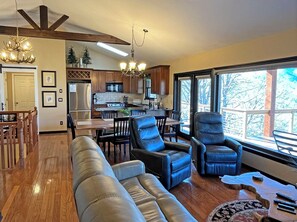 A modern kitchen with wooden cabinets, a dining area with a table and chairs, and a seating area with leather sofas and chairs.