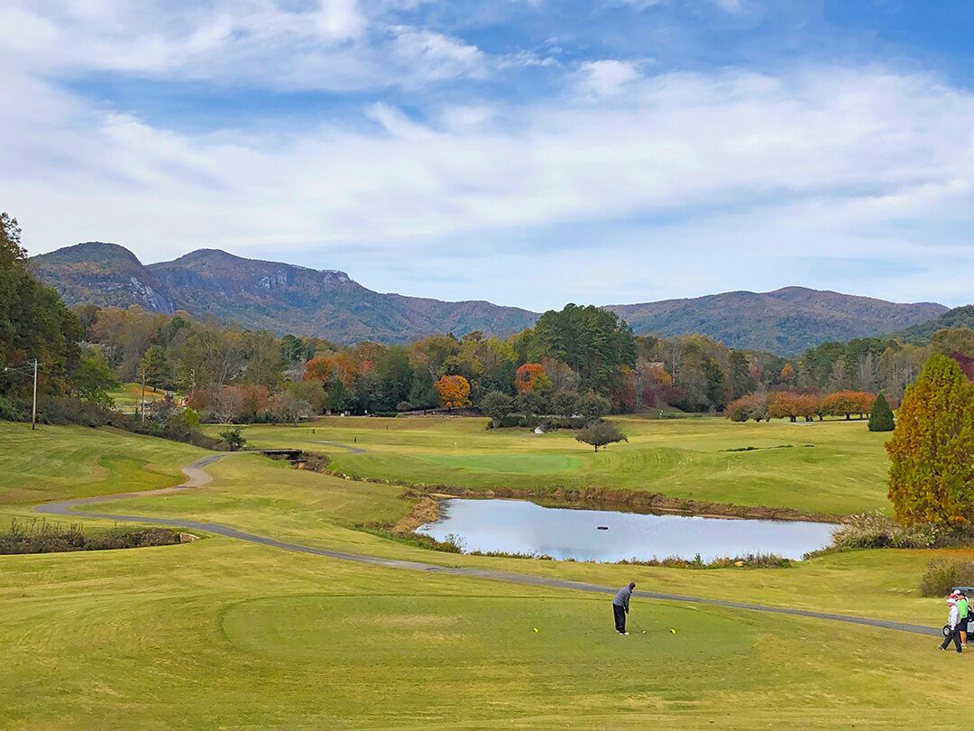 Ein Golfplatz mit Teich, Bäumen und Bergen im Hintergrund.