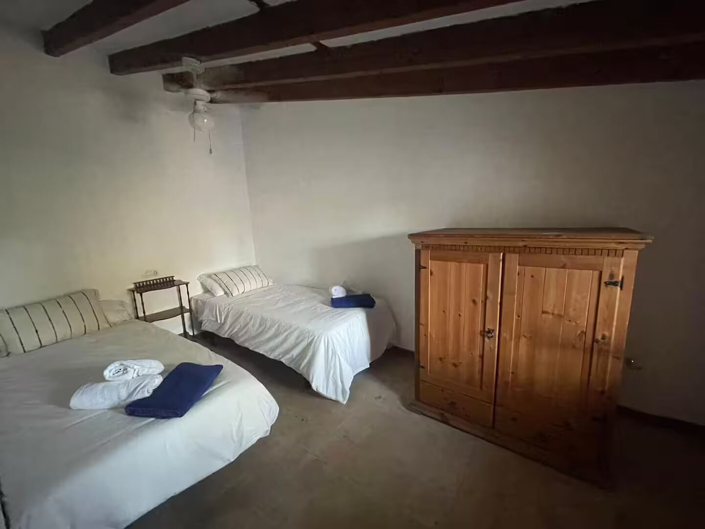 A room with two single beds, a wooden wardrobe, and a ceiling fan.