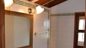 A bathroom with a white sink, a mirror with a decorative frame, and a shower area with tiled walls and floor.