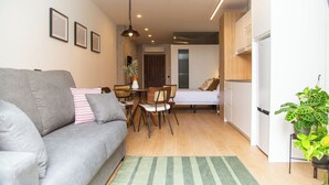 A compact living space with a grey sofa, a dining table with chairs, a small kitchen area, and a bed. - The 153 Hotel (València)