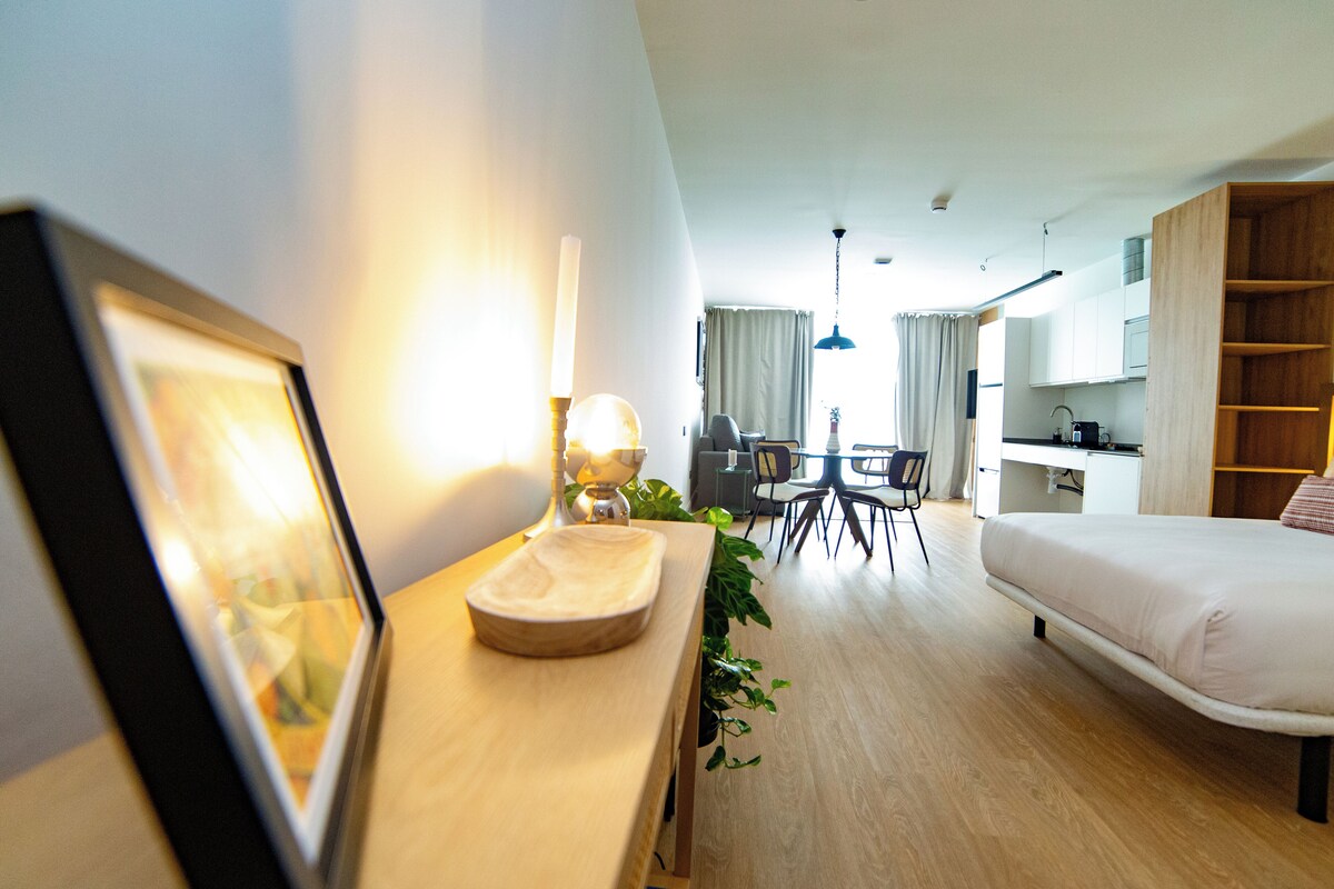 A modern hotel room with a bed, desk, and dining area.