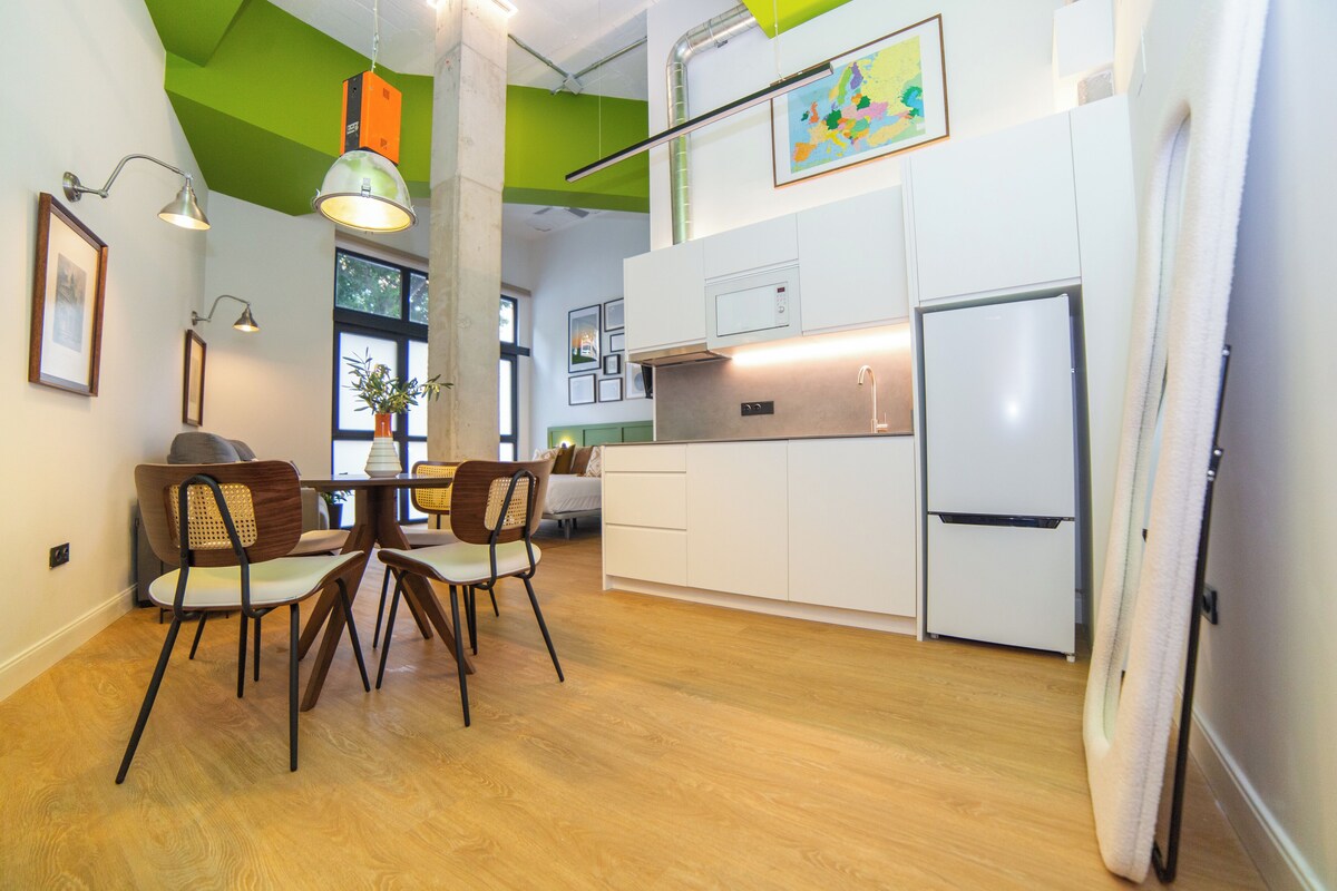 A modern kitchen with white cabinets, a stainless steel refrigerator, and a dining area with wooden chairs and a table.