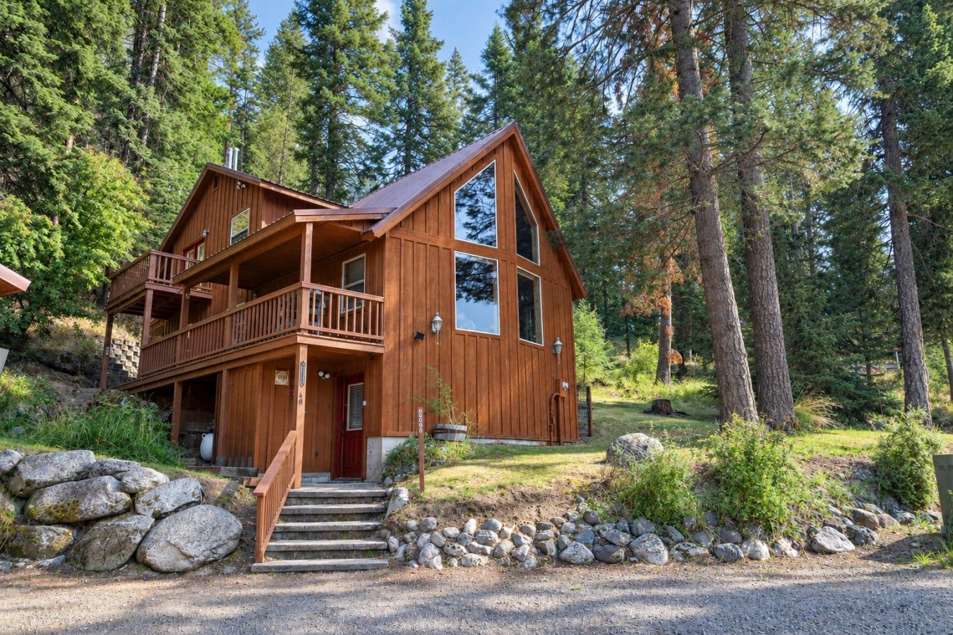 A two-story wooden cabin with a balcony, surrounded by a forest.