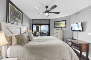 Un dormitorio con cama, ventilador de techo, televisión y vista al exterior.