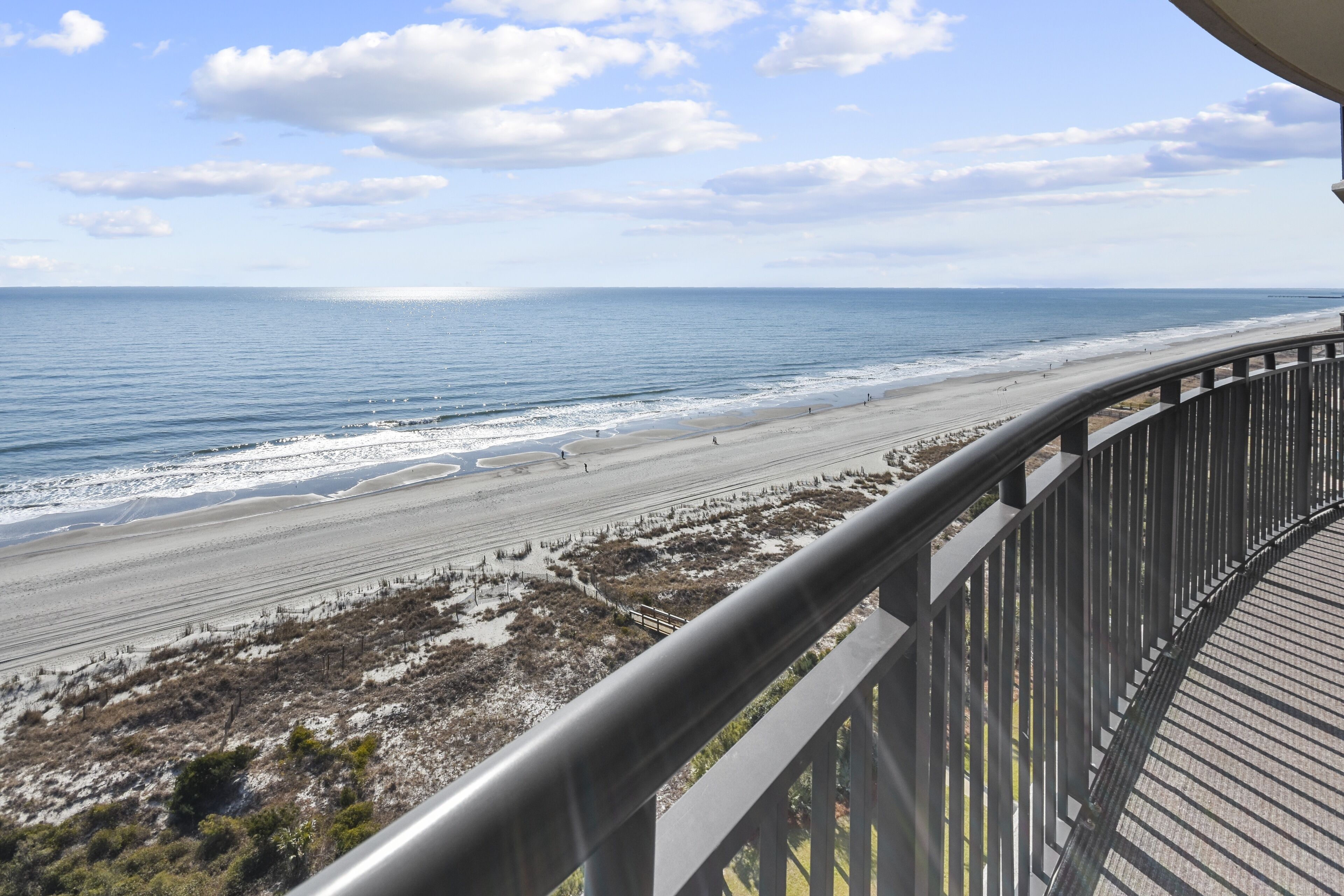 A beach view from a balcony with a railing, sandy beach, and ocean.