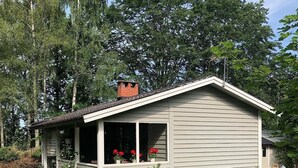 Une maison de plain-pied avec un toit à pignon, une cheminée et une véranda ornée d’une fenêtre où sont exposées des fleurs rouges.