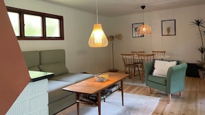 Un salon comprenant un canapé, une table en bois, une table à manger avec des chaises et des luminaires suspendus.