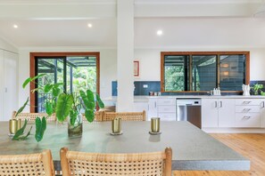 Une cuisine moderne dotée d’un grand îlot central, de meubles blancs et offrant une vue sur la verdure environnante.