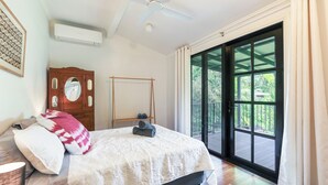 Une chambre avec un lit, une armoire en bois, un ventilateur de plafond et une grande porte-fenêtre coulissante donnant sur un espace extérieur.