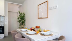 Een moderne keuken met witte kasten, een inbouwoven en een ontbijtgedeekte eethoek met een witte tafel.