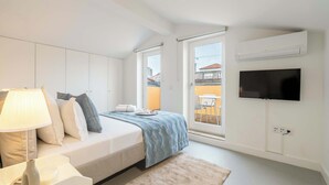 Een moderne slaapkamer met een bed, nachtkastje, lamp en een aan de muur bevestigde televisie.