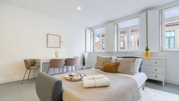 Een moderne slaapkamer met een groot bed, een bureau, twee stoelen en een raam met uitzicht op de stad.