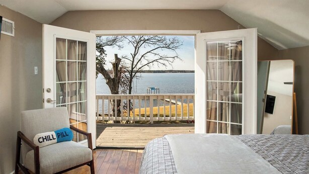 Une chambre à coucher avec un lit, une chaise avec un coussin, une terrasse en bois et une vue sur un lac.