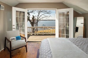 A bedroom with a bed, a chair with a pillow, a wooden deck, and a view of a lake. - ‼️Lakefront Home w/ Dock, BBQ in Peaceful Flint (Flint)