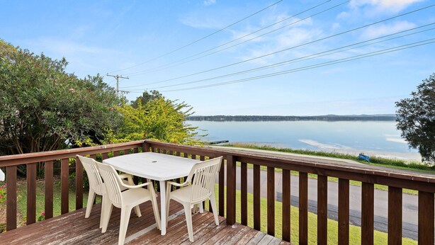 A wooden deck with a table and chairs overlooking a lake. - Lakeside Cottage Escape - Peaceful Stay with Scenic Lake Views (Toukley)