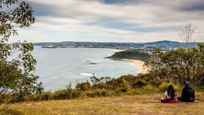 A coastal view with a beach, trees, and a distant town. - Lakeside Cottage Escape - Peaceful Stay with Scenic Lake Views (Toukley)