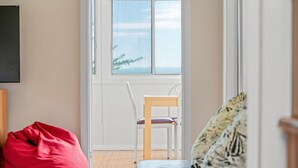 A room with a wooden floor, a white chair, a red bean bag, and a window with a view of trees. - Lakeside Cottage Escape - Peaceful Stay with Scenic Lake Views (Toukley)