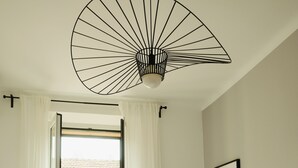 Ein Schlafzimmer mit Bett, Schreibtisch, Stuhl, Heizkörper, einem Fenster mit Vorhängen und Deckenventilator.