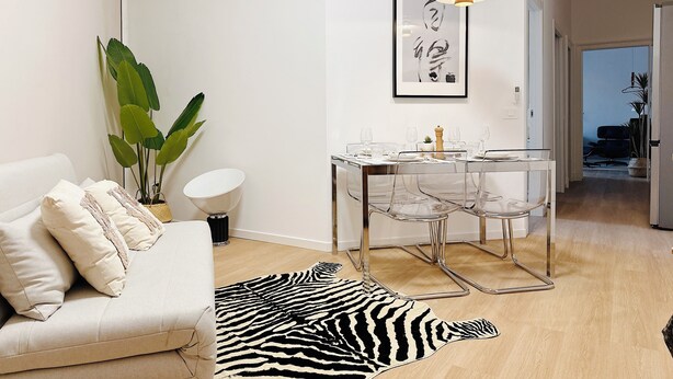 Ein modernes Wohnzimmer mit einer Couch, einem Esstisch mit Stühlen, einem Zebra-Teppich und einer großen Pflanze.