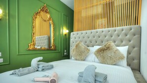Habitación de hotel con pared verde, cabecera capitonada, un espejo grande y una cama con toallas y un secador de pelo.