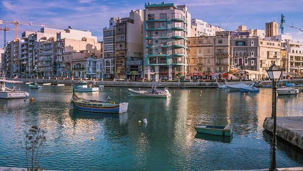 Zona costera con edificios, barcos y una masa de agua tranquila.