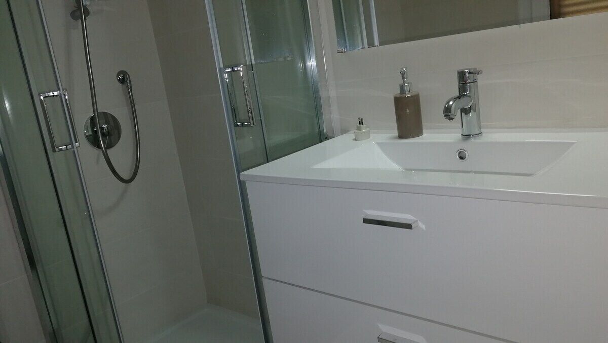 A bathroom with a white sink, a mirror, and a glass shower enclosure.
