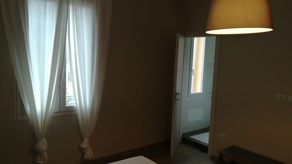 Ein Zimmer mit einer Tür zu einem anderen Raum, einem Vorhangfenster und einer Hängelampe.