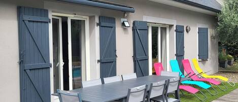 A house with a covered patio, a dining table with chairs, and colorful lounge chairs.