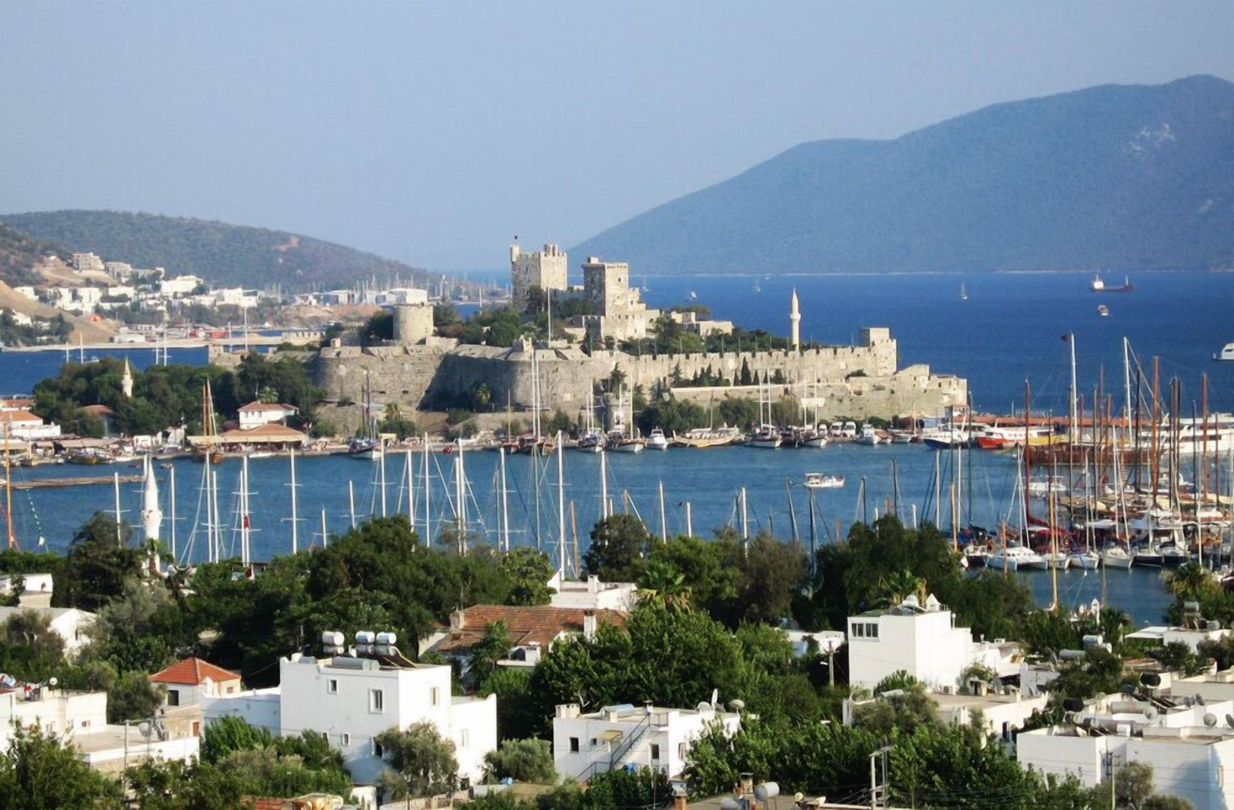 A coastal town with a historic castle, marina with boats, and residential buildings.