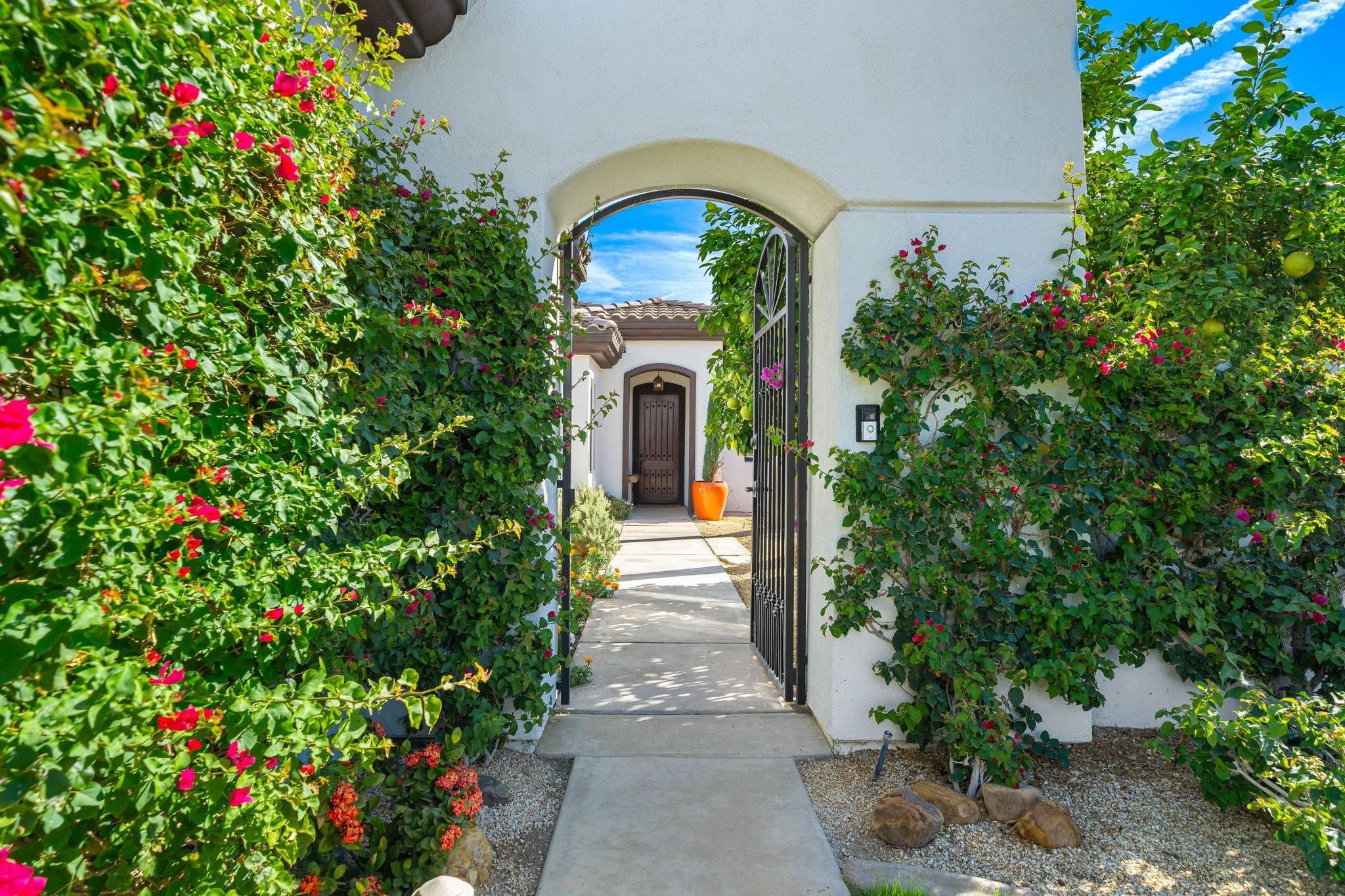 A pathway leading to a building with a brown door, surrounded by lush greenery and flowering plants.