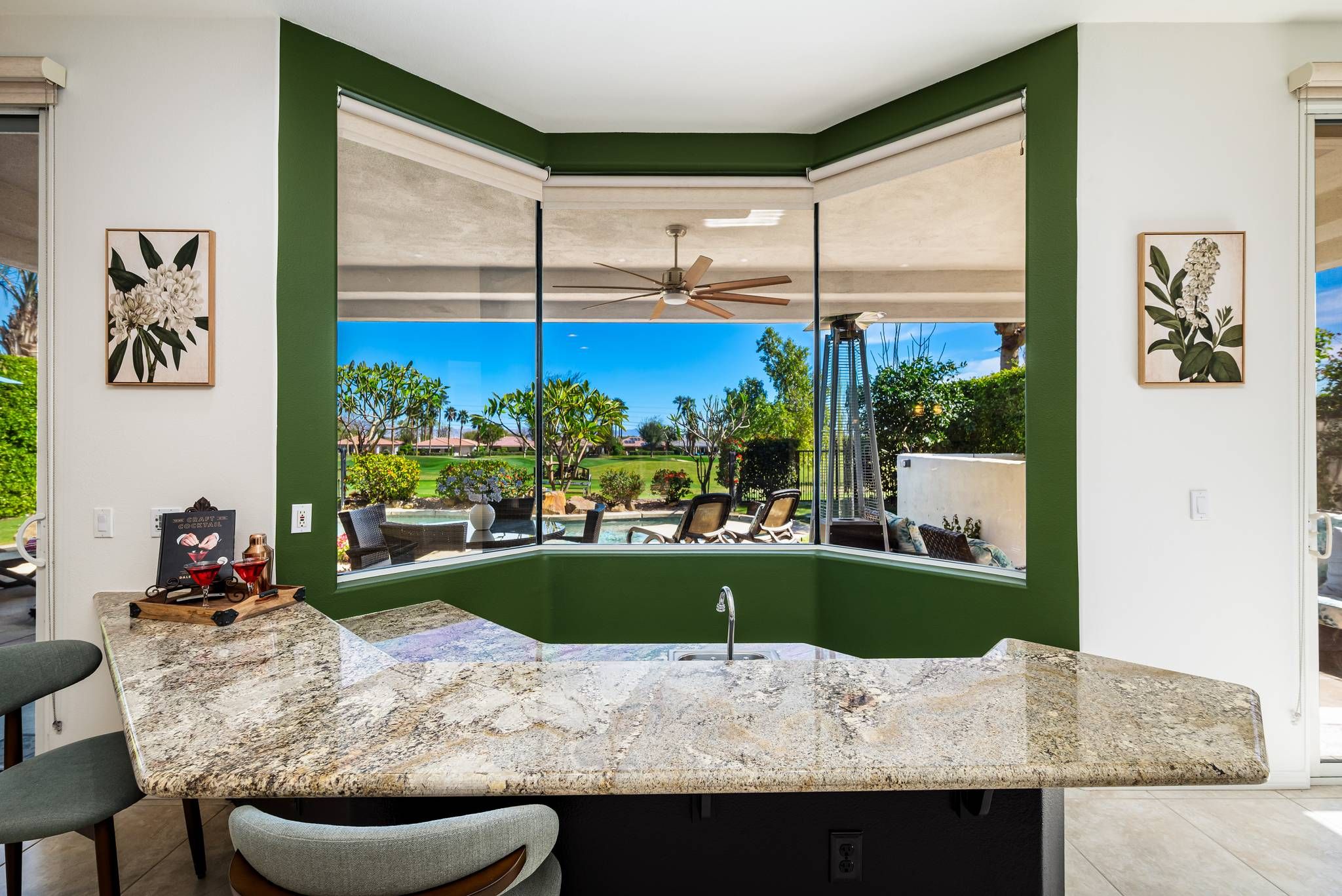 A kitchen with a large island, a ceiling fan, and a view of a backyard with outdoor seating.