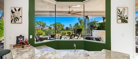 A kitchen with a large island, a ceiling fan, and a view of a backyard with outdoor seating.